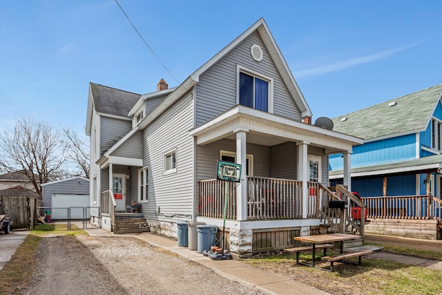 view of front facade featuring a chimney, fence, an outbuilding, a porch, and a garage
