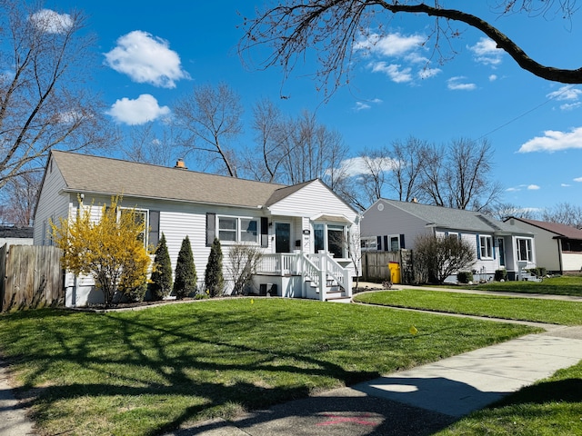 view of front of home with a shingled roof, a front lawn, and fence