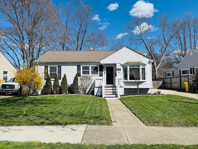 view of front of house with a shingled roof, a front yard, and fence