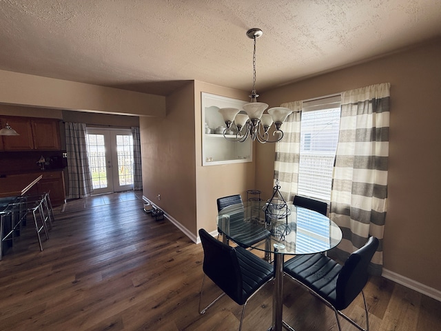 dining space featuring french doors, a textured ceiling, baseboards, a notable chandelier, and dark wood-type flooring