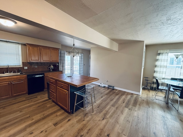 kitchen featuring a textured ceiling, a sink, dark wood finished floors, dishwasher, and tile countertops