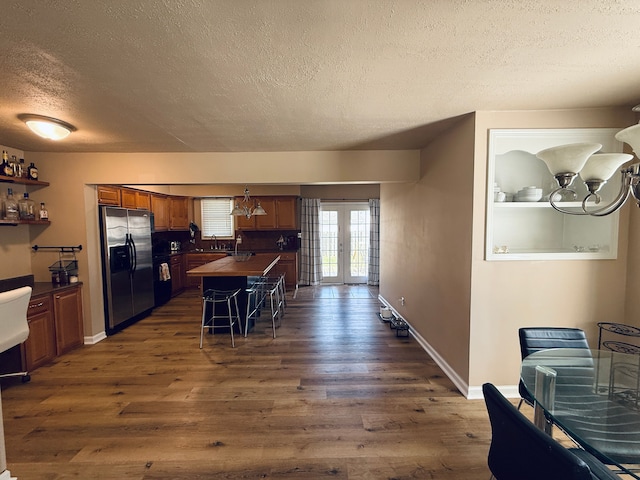 kitchen with a sink, stainless steel fridge, a textured ceiling, a notable chandelier, and dark wood-type flooring
