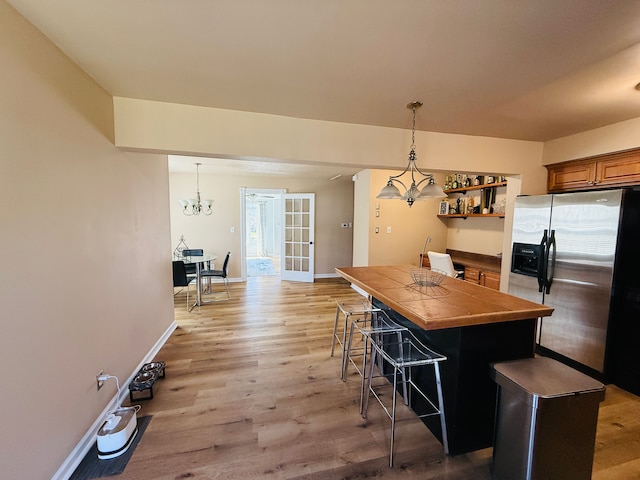kitchen featuring open shelves, tile countertops, a breakfast bar, stainless steel fridge with ice dispenser, and light wood-style flooring
