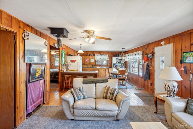 living room with wood walls, ceiling fan, and light wood-type flooring