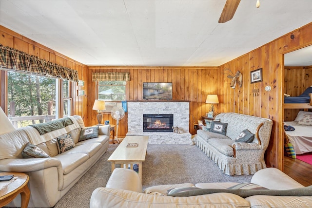 carpeted living room featuring a fireplace, wooden walls, and a ceiling fan