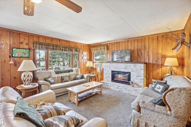carpeted living area with wooden walls, a stone fireplace, and ceiling fan