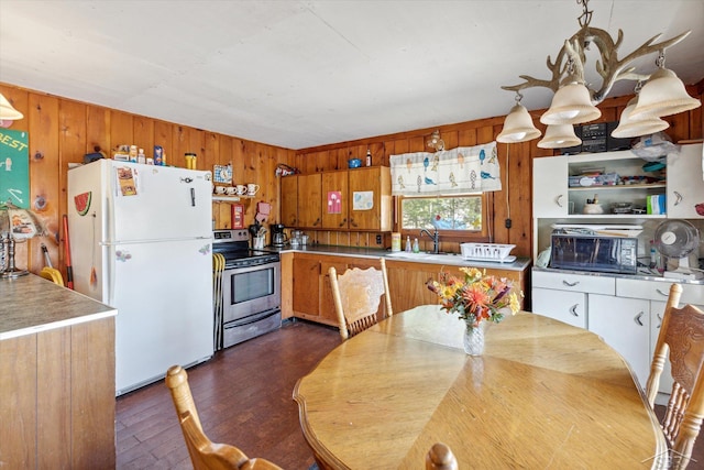 kitchen featuring electric range, freestanding refrigerator, a sink, and wooden walls