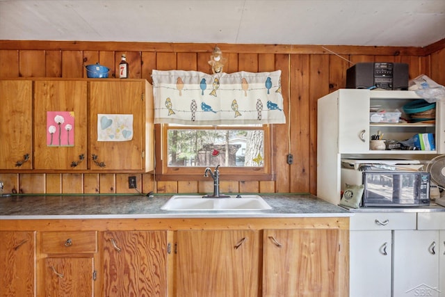 kitchen featuring wood walls, brown cabinetry, and a sink