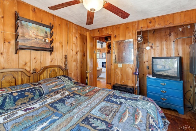 bedroom featuring wood walls, ceiling fan, wood finished floors, and electric panel