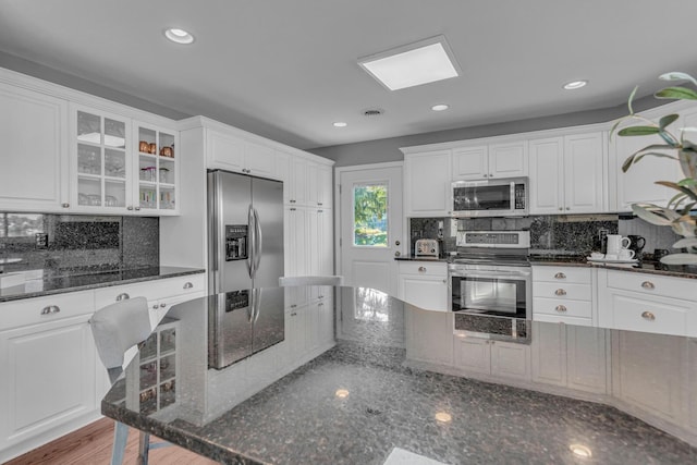 kitchen with glass insert cabinets, white cabinetry, backsplash, and appliances with stainless steel finishes