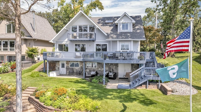 rear view of house with a shingled roof, a yard, stone siding, a patio, and stairs
