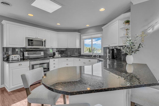 kitchen with a peninsula, white cabinetry, visible vents, stainless steel appliances, and a sink
