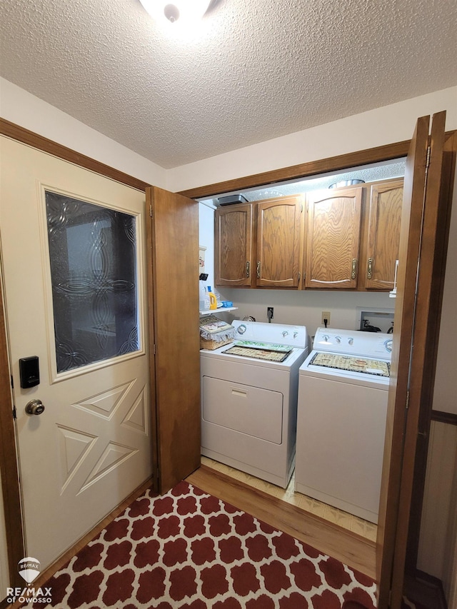 laundry area with cabinet space, washer and clothes dryer, light wood-type flooring, and a textured ceiling