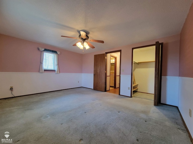 unfurnished bedroom with carpet floors, ceiling fan, a walk in closet, and a textured ceiling
