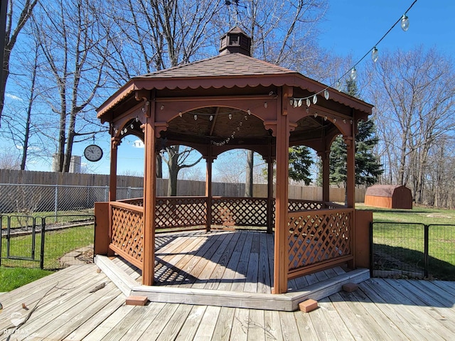 wooden deck with a gazebo, a shed, a fenced backyard, and an outbuilding