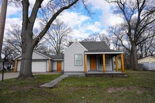bungalow-style home featuring an attached garage, covered porch, and a front lawn