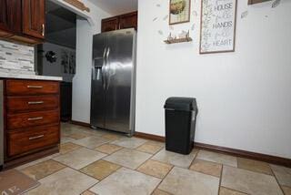 kitchen featuring light countertops, baseboards, stone tile flooring, and stainless steel refrigerator with ice dispenser