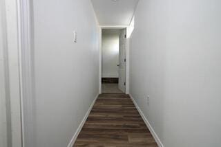 hallway with dark wood-style flooring and baseboards