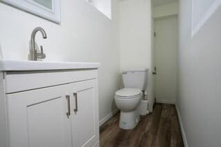 half bath with toilet, vanity, wood finished floors, and baseboards