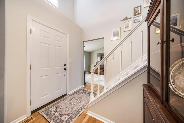 foyer featuring baseboards, a high ceiling, wood finished floors, and stairs