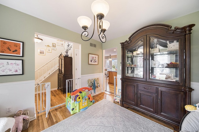 interior space featuring an inviting chandelier, light wood-style flooring, visible vents, a wainscoted wall, and stairs