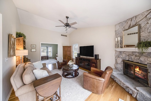 living area featuring a stone fireplace, vaulted ceiling, a ceiling fan, visible vents, and wood finished floors