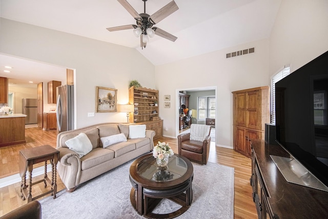 living area featuring baseboards, a ceiling fan, light wood-style floors, visible vents, and high vaulted ceiling