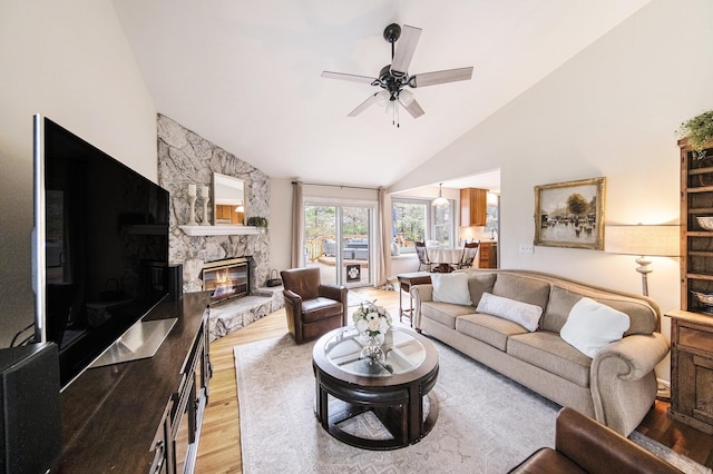 living room with high vaulted ceiling, light wood-style floors, a stone fireplace, and ceiling fan