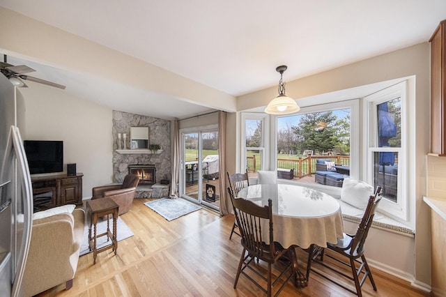 dining space featuring light wood finished floors, a stone fireplace, a ceiling fan, and lofted ceiling