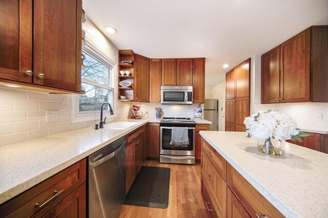kitchen featuring tasteful backsplash, light countertops, light wood-style floors, stainless steel appliances, and a sink