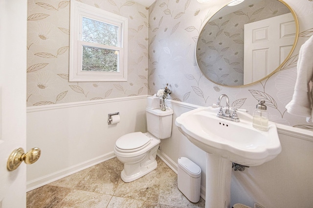 bathroom with toilet, wainscoting, and wallpapered walls