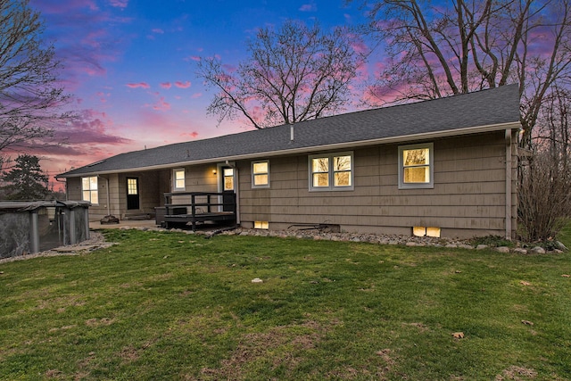 rear view of house featuring a yard, a deck, and roof with shingles