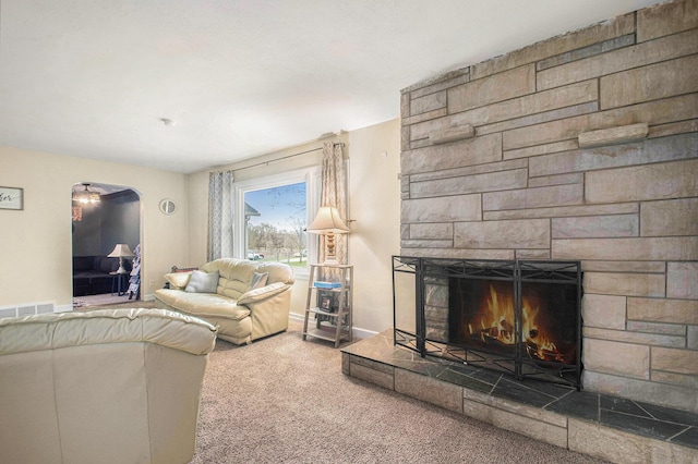 living room with arched walkways, a stone fireplace, visible vents, carpet flooring, and baseboards