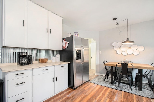 kitchen with arched walkways, stainless steel fridge with ice dispenser, light countertops, and white cabinetry