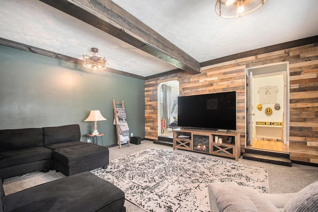 carpeted living room featuring wooden walls, beamed ceiling, a ceiling fan, and arched walkways