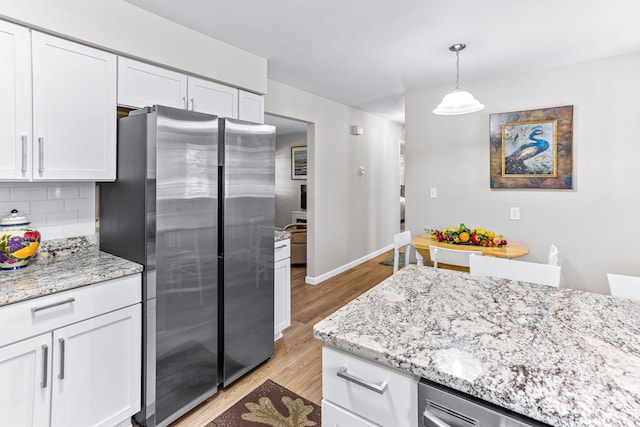 kitchen with white cabinets, light stone counters, light wood-style flooring, freestanding refrigerator, and backsplash