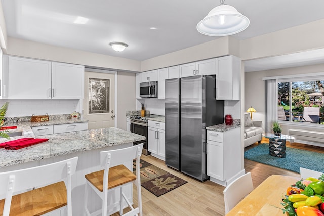 kitchen featuring appliances with stainless steel finishes, tasteful backsplash, light stone countertops, white cabinets, and light wood-style floors