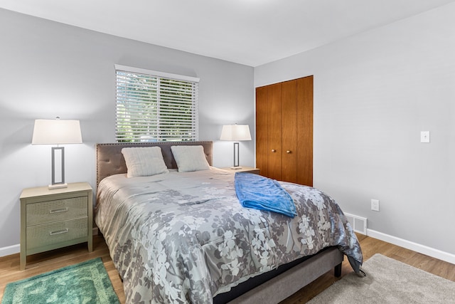 bedroom with baseboards, visible vents, wood finished floors, and a closet