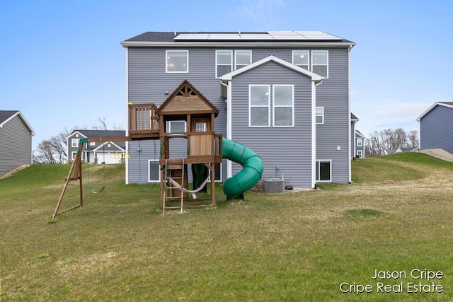 rear view of house featuring a yard, a playground, central AC, and solar panels