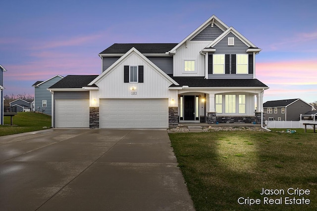 view of front of house featuring an attached garage, stone siding, a lawn, fence, and concrete driveway