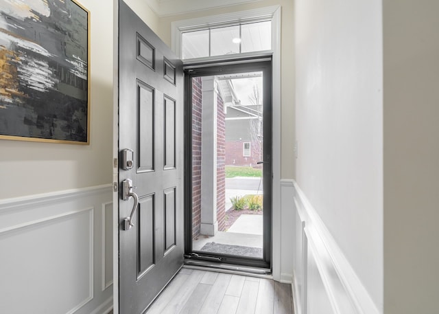 foyer featuring wainscoting, a decorative wall, and light wood-type flooring