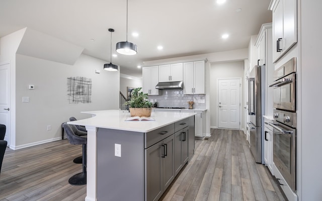 kitchen featuring a center island, light wood-style floors, a breakfast bar, stainless steel appliances, and backsplash