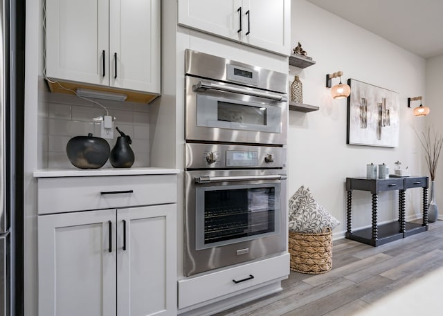 kitchen with tasteful backsplash, stainless steel double oven, light wood-style floors, light countertops, and baseboards