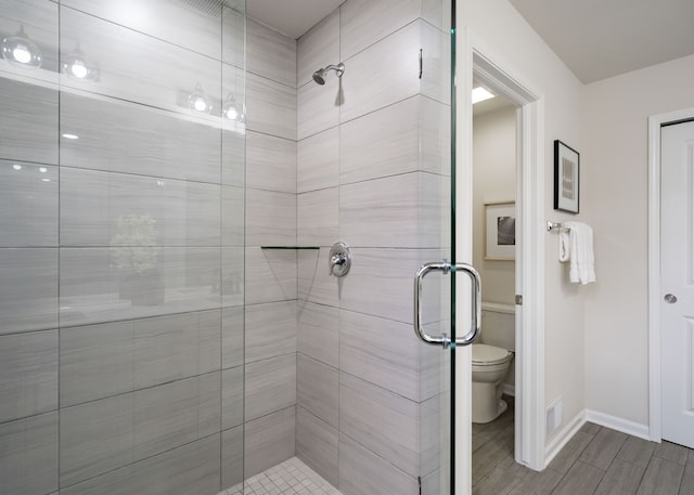 bathroom featuring a shower stall, baseboards, toilet, and wood finished floors