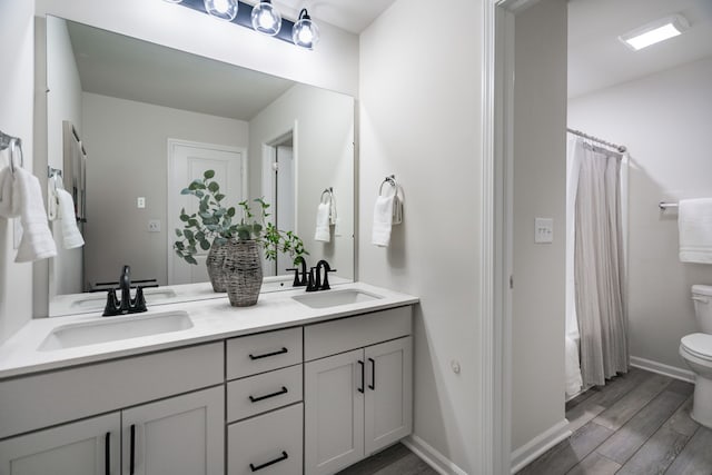 bathroom featuring toilet, wood finished floors, a sink, and double vanity