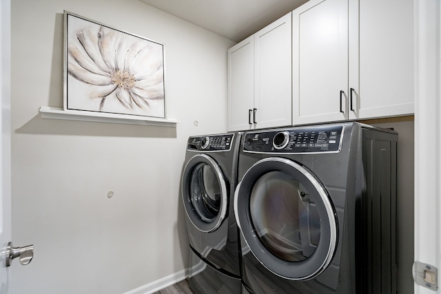 clothes washing area with washing machine and dryer, baseboards, and cabinet space