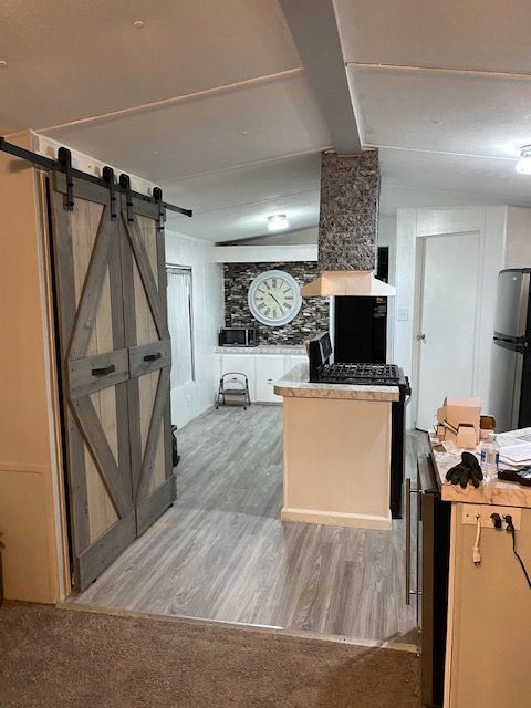 50594 Oregon Ave, Novi, MI 48374 - kitchen featuring light wood-type flooring, wall chimney range hood, a barn door, appliances with stainless steel finishes, and decorative backsplash