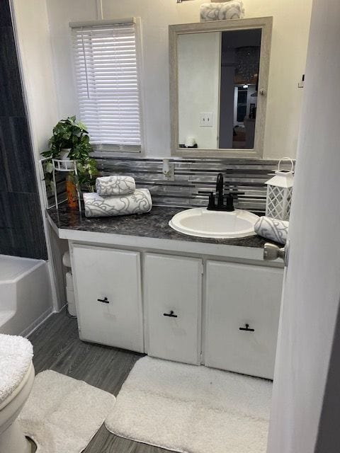 50594 Oregon Ave, Novi, MI 48374 - full bathroom with vanity, toilet, decorative backsplash, a tub to relax in, and wood finished floors