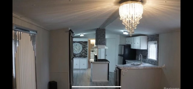 50594 Oregon Ave, Novi, MI 48374 - kitchen with freestanding refrigerator, white cabinetry, vaulted ceiling, a sink, and a notable chandelier