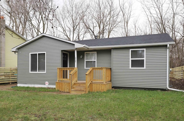 back of property with a yard, fence, and roof with shingles